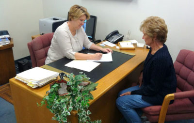 Two women sitting at a desk in front of each other.