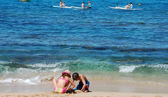 Two people on the beach near water and a body board.